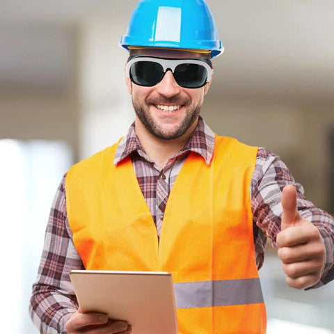 Smiling worker in safety gear wearing Kickass Protective Eyewear And Safety Glasses With Lenses For Welders, bright orange vest, blue helmet.