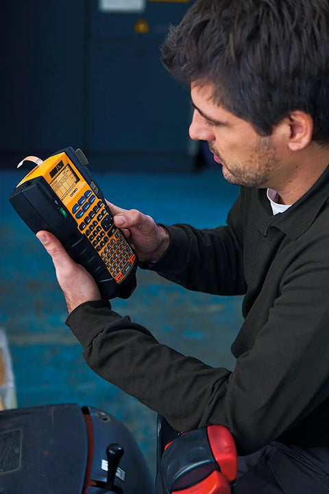 Man using Rhino 5200 Label Maker With One Touch Hot Keys for speedy, durable asset labeling on job sites, printing barcodes.