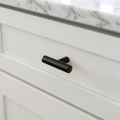 Matte black cabinet knob on a white drawer, part of 25 Pack Premium Matte Black Cabinet Knobs And Slick Drawer Pulls With 2 Inch Round Profile For Zero Hassle Kitchen Update Including All Mounting Hardware For Fast Swap.