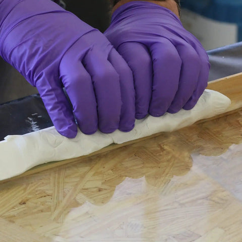Applying Ready To Use White Window Glazing Compound 32 Oz Tube for sealing gaps with purple gloves on wooden surface.