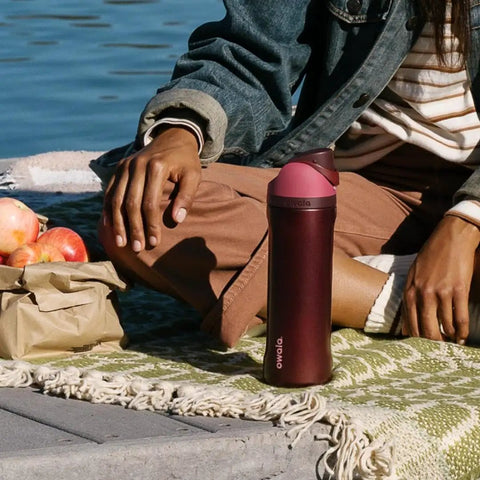 Heavy Duty Double Walled Stainless Steel Water Bottle 24 Oz next to a person enjoying a picnic with apples by the water.
