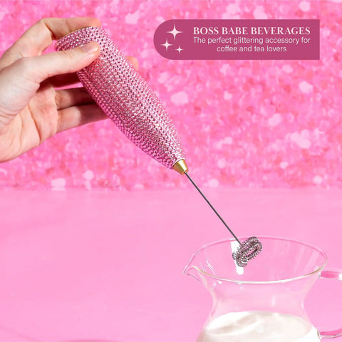 Electric Rhinestone Handheld Milk Frother With Double Coil Whisk And Gold Stand in use above glass of milk on pink background