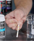 Real Down To Earth Five In One Water Quality Test Strips For Pools And Spas shown with a beaker and testing strip held in hand.
