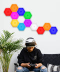 Hexagon LED Wall Panels 10 Pack With Remote And Touch Control RGB 13 Color Lights arranged on a wall above a seated person.