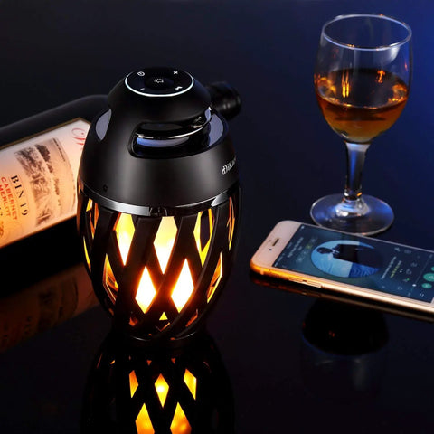 LED Flame Outdoor Table Lamp With Bluetooth Speaker Rechargeable Ambience Lantern With Flickering Warm Light beside wine and phone.