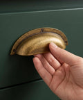 Transform Your Kitchen Setup With 3 Inch Antique Brass Cup Pulls Heavy Duty Solid Zinc Alloy Drawer Handles Vintage Home Office Cabinet Knobs 6 Pack. Hand grasping a vintage brass cup pull on green drawer.