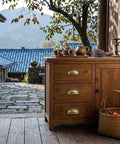 Antique brass cup pulls on a wooden cabinet with a rustic design, featuring three drawers, complementing a home setting.