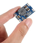 Person holding a compact Five Volt Five Amp Mini560 Buck Converter Module For DIY Projects, showing blue circuit board and components.