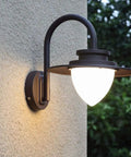 Heavy Duty One Light Outdoor Wall Lantern And Porch Light Featuring Round Pe Lens Dark Brown Die Cast Aluminum Body With Anti Uv Powder Coat That Shoulders Bad Weather Like A Champ While Keeping Your Porch Lookin Fresh For Neighborhood Hangouts mounted on textured wall with soft glow.