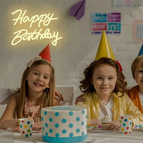 Children celebrating in front of a lit adjustable dimmable Happy Birthday neon sign LED light backdrop, polka dot cake on table.