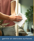 Side view of a person wiping a mirror with a white microfiber cleaning cloth.
