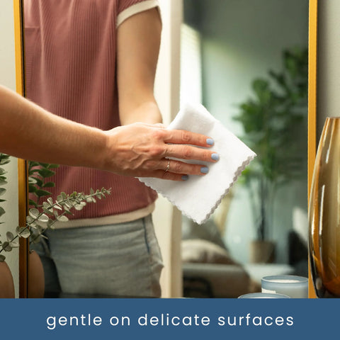 Side view of a person wiping a mirror with a white microfiber cleaning cloth.