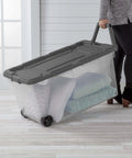 Rugged Pull Along 160 Quart Rolling Storage Tote With Transparent Bottom carrying blankets and pillows on wheels.