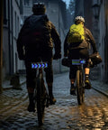 Cyclists with programmable LED smart bike tail light with speedometer and app control, displaying patterns on cobblestone road.