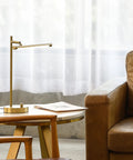 West 15 Inch LED Integrated Desk Lamp in Matte Brass with pivoting head on side table, near sofa
