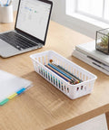 Eighteen Pack Slick Slim Plastic Baskets For Narrow Drawer Setup with office supplies on a desk, 10 x 3 inch white storage tray.
