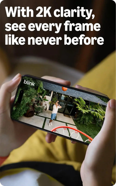 Person watching live feed of outdoor camera on smartphone, showcasing Top Tier Wireless Home Security Bundle With Crisp 2K Plus Outdoor Camera And Reliable Video Doorbell Featuring Hella Long Battery Life And No Sweat Smart Motion Alerts For Solid Protection Around Your Pad.