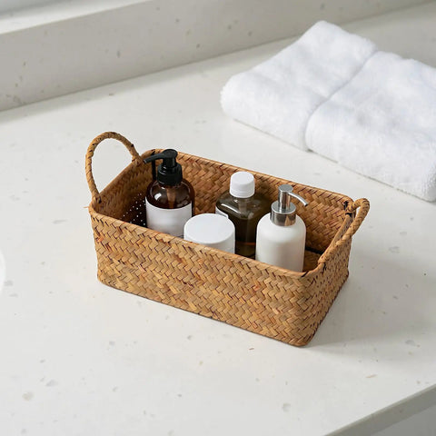 Spacious Open Top Seagrass Woven Storage Basket With Heavy Duty Handles For Kitchen Farmhouse Pantry Bathroom Towels Cosmetics And Hassle Free Daily Organization Goals on a countertop with toiletries.
