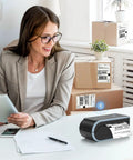 Bluetooth Thermal Label Printer With Built In Paper Bin Wireless Shipping Label Printer For iOS Android Windows Mac ChromeOS USB Or Bluetooth Connection Ideal For Etsy Shopify USPS And Small Biz next to smiling woman in office setting