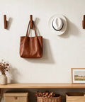 Rock-Solid Natural Walnut Wood 4 Pack Wall-Mounted Coat Hooks with a leather bag and hat against a light wall.