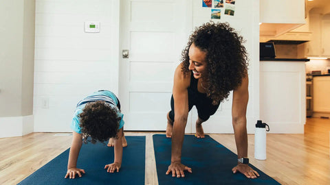 Room with a family exercising, visible on the wall is a Programmable Thermostat With One Week Programming And Digital Display White.