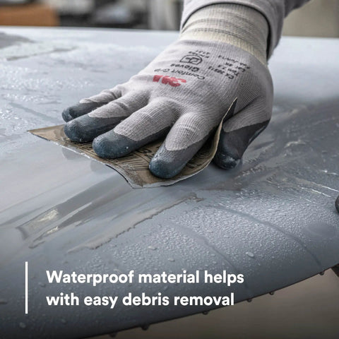 Gloved hand using Pro Grade Wetordry Abrasive Sheets 401Q 1200 Grit 9 By 11 Inches Pack Of 50 on wet car surface for sanding.
