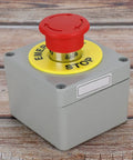 Rugged One Button Emergency Stop Switch Box With Red Push Button IP66 Enclosure Aluminum Die Cast Housing Normally Closed Industrial Grade Stop Button Box Built For Harsh Environments 80 By 75 By 60 Mm on wooden surface.