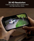 Hands holding smartphone showing footage from Outdoor Floodlight Security Camera 2K HD With Color Night Vision, 2800-Lumen LEDs.