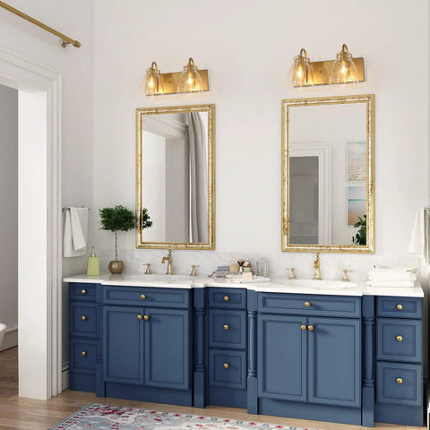 Bathroom with two Light Gold Vanity Light Fixtures, clear glass shades, modern bronze backplane over dual sinks with blue cabinets.