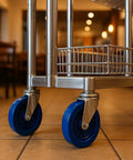 Five Inch Stainless Steel Casters Four Pack Heavy Duty Industrial Roller Mounts Two Swivel With Top Lock Brakes And Two Rigid Wheels 1400 Pound Capacity Blue Non Marking Urethane Tires For Carts Built Tough For Smooth Rollin on a cart floor.