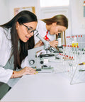 Two female scientists using microscopes in a lab with a Solid 24 Position Lab Test Tube Drying Rack With Plastic Coated Metal.