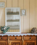 Elegant rustic wooden dresser with a white-framed mirror and decorative flowers and stone accent against a paneled wall.