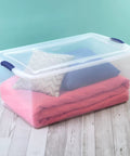 Super Size 105 Quart Clear Plastic Storage Bin With Blue Latching Lid For Big Hauls And House Decluttering with blankets and pillows.