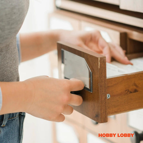Person using floral drawer knob to open wooden cabinet drawer, showcasing easy access and stylish design.