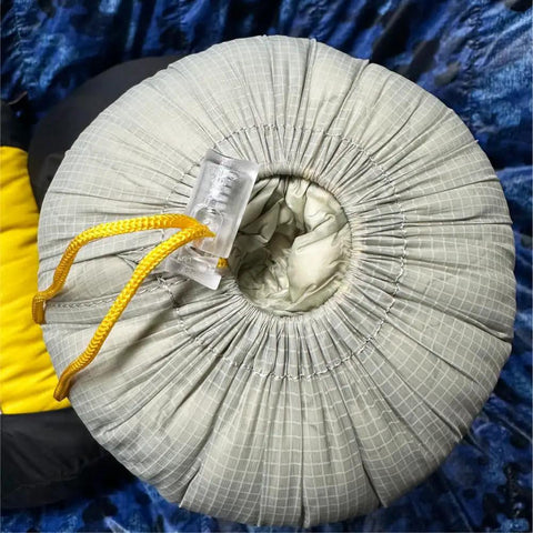 Top view of ultra-light water resistant compression stuff sack for sleeping gear, teal nylon with yellow drawstring, outdoors.