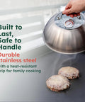 Hand using 12 Inch Stainless Cheese Melt Dome With Glass Lid And Built In Thermometer Up To 700 F Steam Vent For Faster Melts On Burgers And Veggies The Go To For Flat Top Griddles BBQ And Hibachi Grills over burgers.