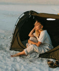 Person sitting in a tent at sandy beach, no visible LED Camping Lantern Round Waterproof Portable Tent Light for Hiking and Emergencies