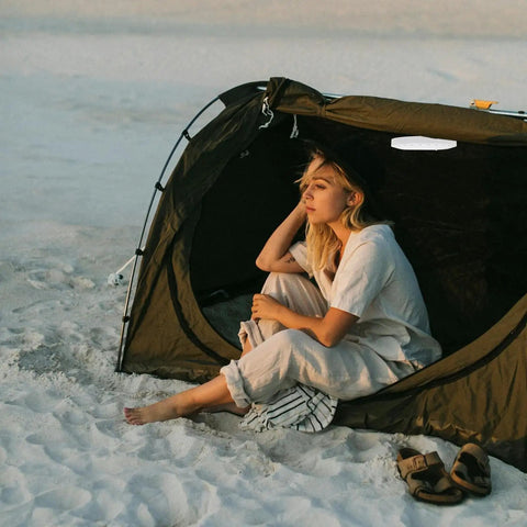 Person sitting in a tent at sandy beach, no visible LED Camping Lantern Round Waterproof Portable Tent Light for Hiking and Emergencies