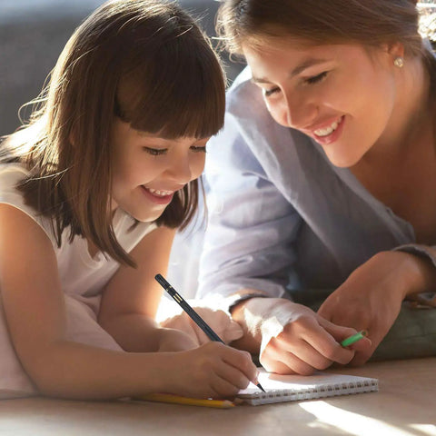 Smiling child drawing in a notebook with an adult assisting, using charcoal pencils for drawing set 10 pack.