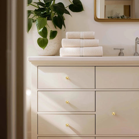 Rock Solid Zinc Alloy Cabinet Pulls Featuring A Slick Brushed Gold Finish 1 1/4 Inch Diameter on dresser with stacked towels.
