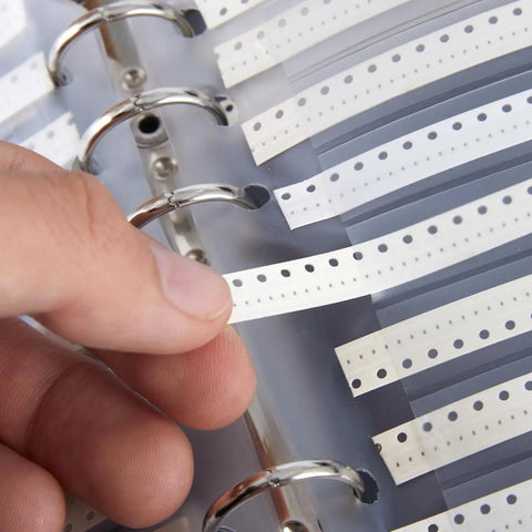Person's hand selecting labels from Top Shelf SMD 0201 Capacitor Kit Packing 2550 Surface Mount Chips With Broad Values From .5Pf To 220Nf.