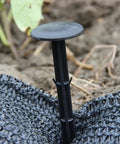 6 inch plastic tarp stake anchoring garden netting on soft ground, part of a 30 pack heavy duty yard stakes set.