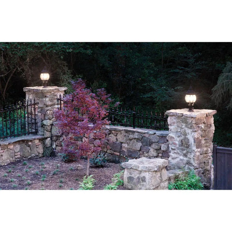 Stone wall with lantern lighting and decorative wrought iron fencing in a garden setting at dusk, showcasing exterior decor.