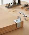 Compact Right Angle Corner Bracket For Woodworking Metal Frame Brace Plate attached to wooden edge with workshop tools