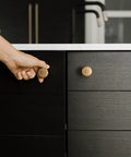 Hand reaching for a 6 Pack Amber Red Cabinet Knobs 1.3 Inch Zinc Alloy Drawer Pulls Featuring Floral Radiating Texture on black cabinet.