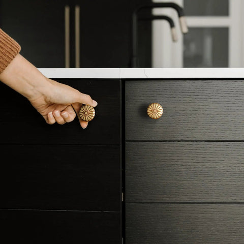 Hand reaching for a 6 Pack Amber Red Cabinet Knobs 1.3 Inch Zinc Alloy Drawer Pulls Featuring Floral Radiating Texture on black cabinet.