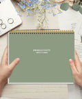 Person holding Weekly Productivity Planner Notepad For Busy Pros, 8.5 By 11 Inch Dashboard Organizer With Six Focus Areas, Green cover.
