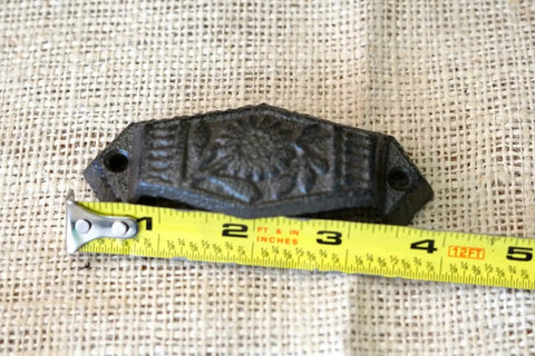 Close-up of a vintage cast iron cup pull measuring 4 inches, detailed with a floral design for drawer hardware.