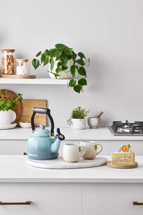 Enamel On Steel Demi Tea Kettle 1.25 Qt Sea Salt Finish With Whistle on kitchen countertop with mugs and cake