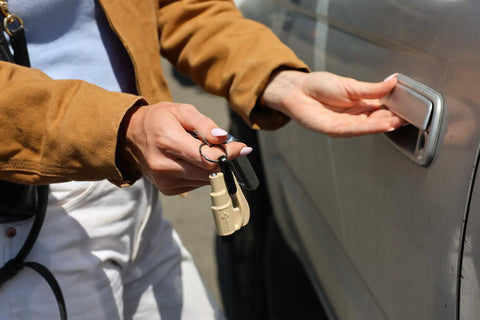 Straight Up Solid Car Escape Keychain With Seatbelt Cutter And Tempered Glass Window Breaker Made In Usa held by a person near a vehicle.